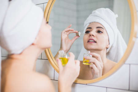 Young woman in white towel apply moisturising oil on face skin.の写真素材
