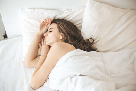 Young woman sleeping peacefully in bedroom with white fresh sheetsの写真素材