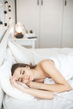 Young woman sleeping peacefully in bedroom with white fresh sheetsの写真素材
