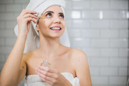 Young woman in white towel apply moisturising oil on face skin.の写真素材