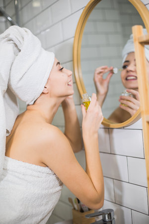 Young woman in white towel apply moisturising oil on face skin.の写真素材