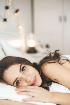 Beautiful young woman waking up in comfortable bed on white fresh sheets.の写真素材