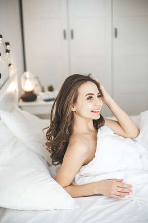 Beautiful young woman waking up in comfortable bed on white fresh sheets.の写真素材