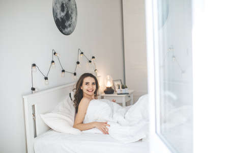 Beautiful young woman waking up in comfortable bed on white fresh sheets.の写真素材