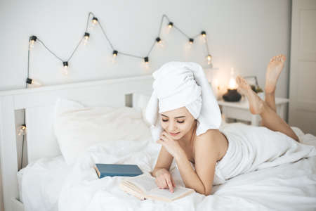 Young happy woman reading paper book in bed.の写真素材