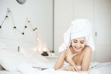 Young happy woman reading paper book in bed.の写真素材