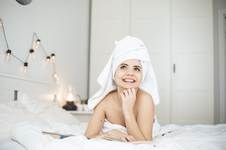 Young happy woman reading paper book in bed.の写真素材