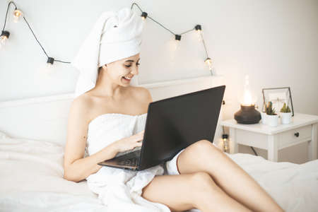 Young woman working in white bed using laptop.の写真素材