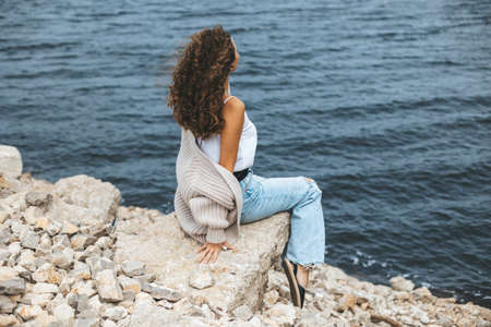 Young woman from behind sitting on rocky river bankの写真素材