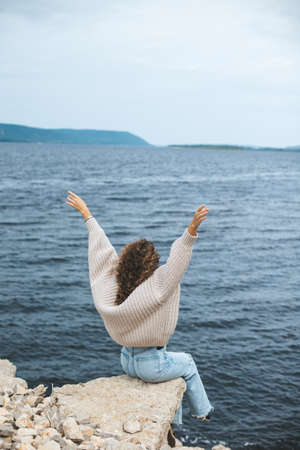 Young woman from behind sitting on rocky river bankの写真素材