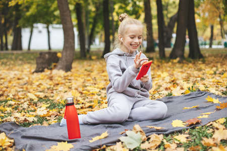 Gen z teenage girl using smartphote outdoors in autumn time.の写真素材