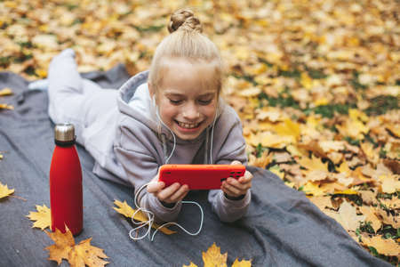 Gen z teenage girl using smartphote outdoors in autumn time.の写真素材