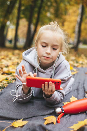 Gen z teenage girl using smartphote outdoors in autumn time.の写真素材