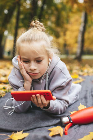Gen z teenage girl using smartphote outdoors in autumn time.の写真素材