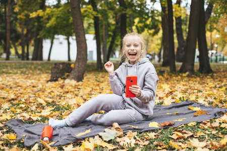 Gen z teenage girl using smartphote outdoors in autumn time.の写真素材