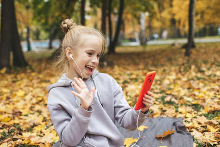 Gen z teenage girl using smartphote outdoors in autumn time.の写真素材
