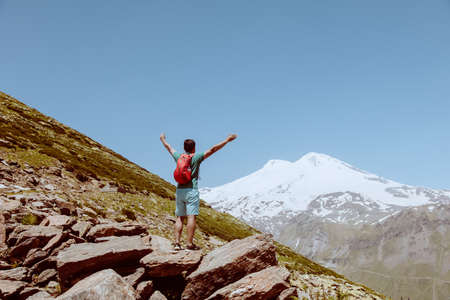 Man with red backpack stand on rocky mountain and look at snowy peak of Elbrus.の写真素材