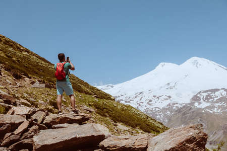Man with red backpack stand on rocky mountain and look at snowy peak of Elbrus.の写真素材