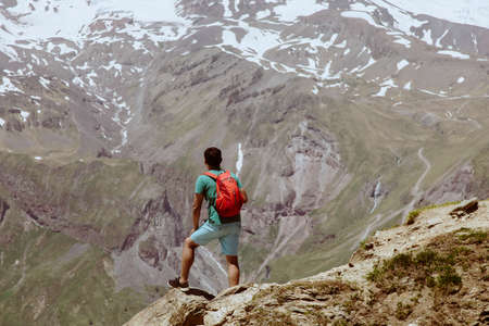Man with red backpack stand on rocky mountain and look at snowy peak of Elbrus.の写真素材