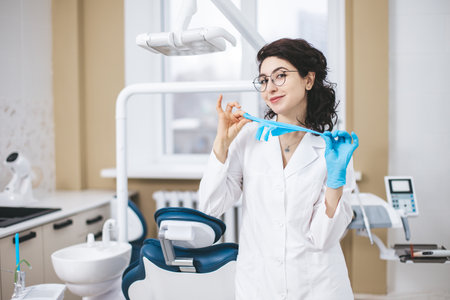 Professional young dentist posing confidently beside modern dental equipment in a dental clinic. Portrait of female doctor.の写真素材