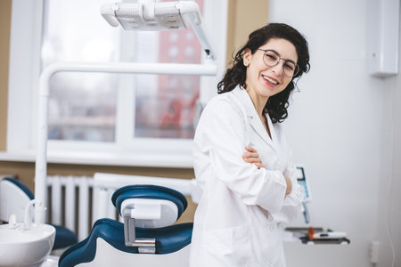 Professional young dentist posing confidently beside modern dental equipment in a dental clinic. Portrait of female doctor.の写真素材