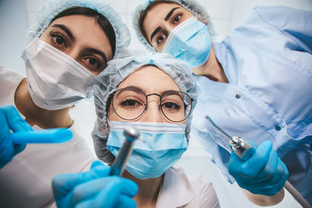 Tree female dentists examining patients mouth from above using medical equipment.の写真素材