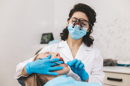 Female dentist examining patients mouth using stomatological binoculars. Using modern technologies in medicine.の写真素材