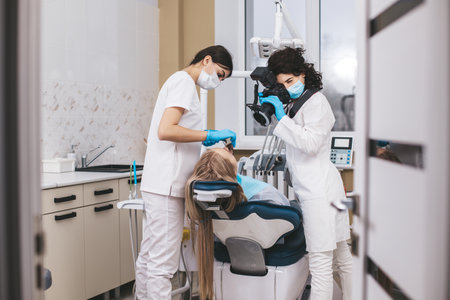 Female dentist with camera making shots of patients smile after treatment using special shadowless camera with flash ring. Medical assistant holding mirror.の写真素材