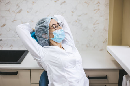 Female doctor in medical mask sitting on dentist chair after working day. Portrait of a woman stomatologist in clinic office.の写真素材