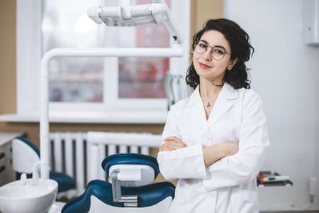 Professional young dentist posing confidently beside modern dental equipment in a dental clinic. Portrait of female doctor.の写真素材