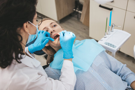 Female dentist examining patients teeth on dentist chair, view from patients side.の写真素材