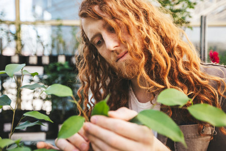 Red haired botanist examines plant leaves in a lush greenhouse, showing dedication to plant care and horticulture. The scene captures sustainable farming, highlighting nature and growthの写真素材
