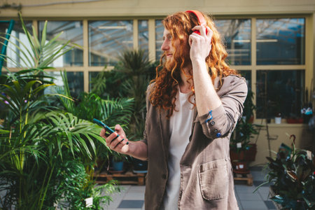 A man with red hair is holding a cell phone and wearing headphones. He is smiling and he is enjoying his music via smartphone.の写真素材