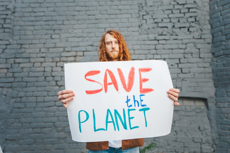 A man holding a sign that says Save the Planet on gray brick background wall. Anti pollution protest, eco activism and earth protection concept.の写真素材