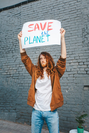 A man holding a sign that says Save the Planet on gray brick background wall. Anti pollution...