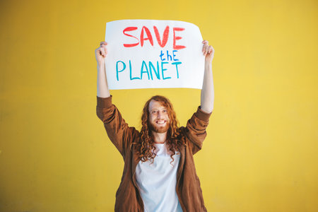 A man holding a sign that says Save the Planet on yellow background wall. Anti pollution protest, eco activism and earth protection concept.の写真素材