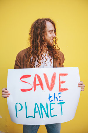 A man holding a sign that says Save the Planet on yellow background wall. Anti pollution protest, eco activism and earth protection concept.の写真素材
