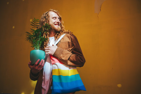 Confident man with long red hair holds a plant and rainbow bag, symbolizing pride and individuality in the lgbtq community. Vibrant portrait captures modern, eco friendly urban lifestyleの写真素材