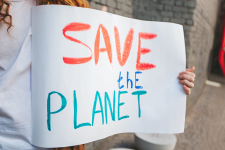 Young activist holds a save the planet sign at a climate change protest, surrounded by marchers demanding action against global warming and pollutionの写真素材
