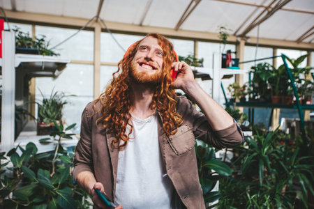 A man with red hair is holding a cell phone and wearing headphones. He is smiling and he is enjoying his music via smartphone.の写真素材