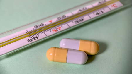 two capsules of medicine lie next to a medical thermometer