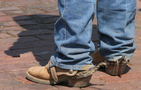 Legs of cowboy showing boots with longhorn spurs and shadow of cowboy