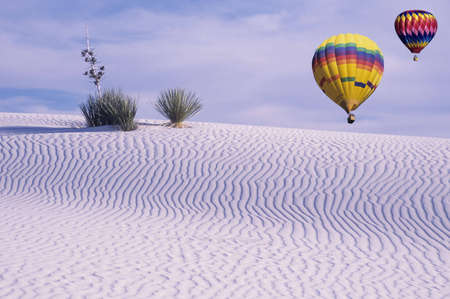 Two hot air balloons floating over white sands with soaptree yuccaの写真素材