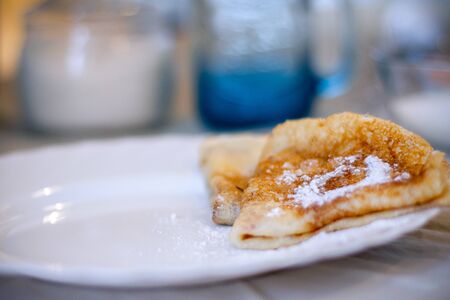 Pancakes on a white plate with powdered sugar, served for Breakfast, Cutlery and dishes in the...