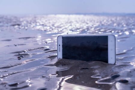 Smartphone stuck in the wet sand of the beachの写真素材