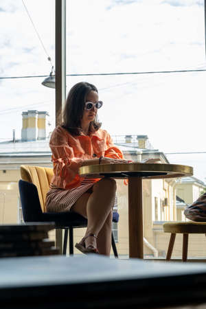 Young Caucasian Woman in Sunglasses Reading Book at Table in a Coffee shop
