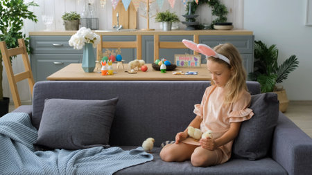 Caucasian Little Girl Sitting on Sofa and Playing with Chickens on Decorated Kitchen for Easterの写真素材