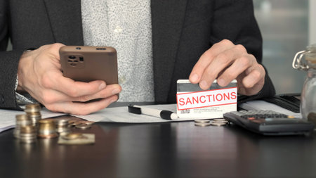 Nervous Man Having Financial Difficulties Due to Sanctions, Holding Bank Card and Using Smartphone,...
