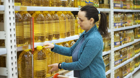 Young Woman Buys Big Bottles of Sunflower or Olive Oil in Grocery Store, Putting it into Shopping Cart. Hoarding, Economic Crisis and Food Shortageの写真素材