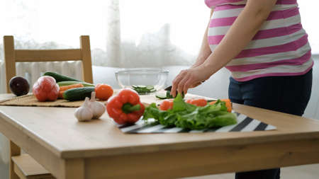 Closeup of Pregnant Woman Doing Green Salad, Cutting Organic Cucumber on the Wooden Board. Healthy Food and Nutrition for Expectant Motherの写真素材